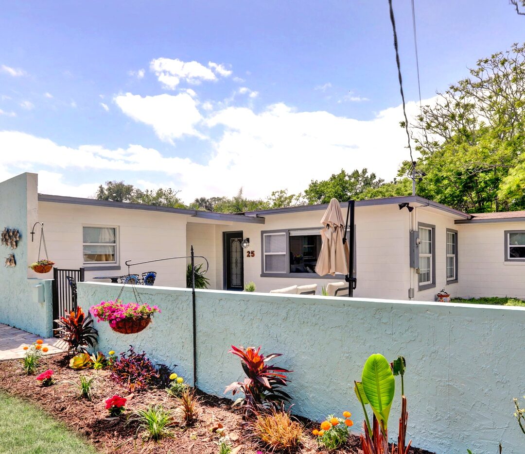 Fenced front courtyard with tropical landscaping and flower beds