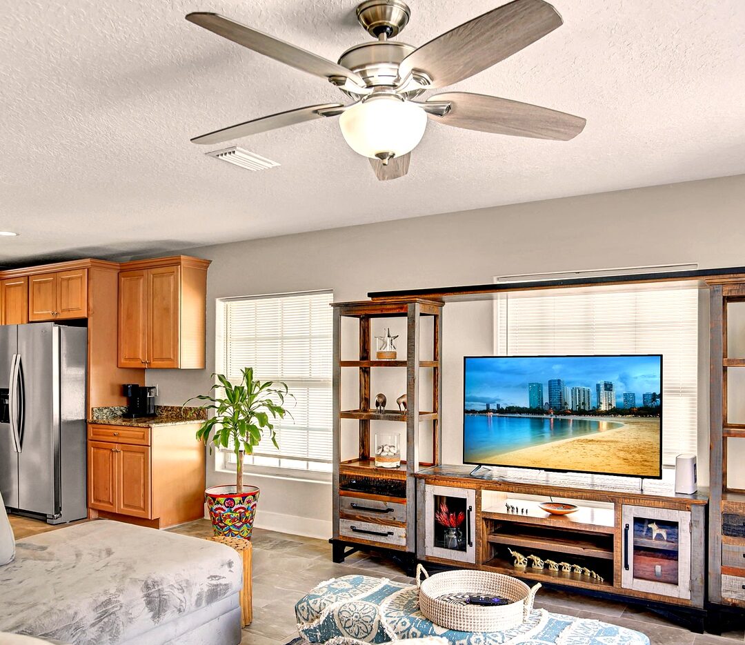 Living room with tile floors, ceiling fan, and view into the kitchen with stainless refrigerator
